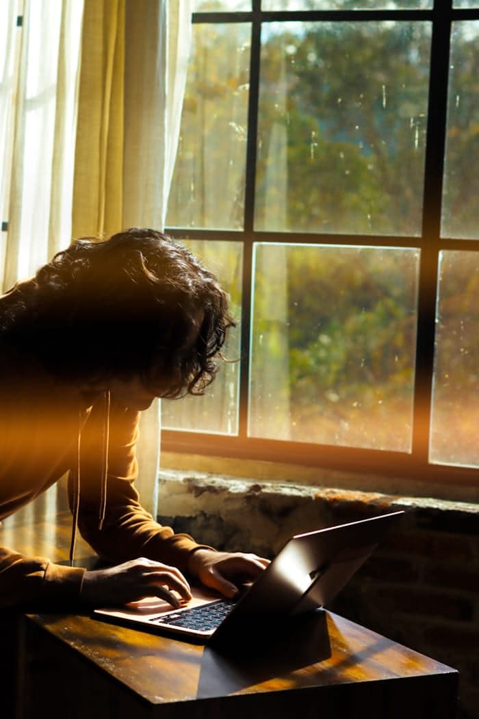 A person working on a laptop by a sunlit window